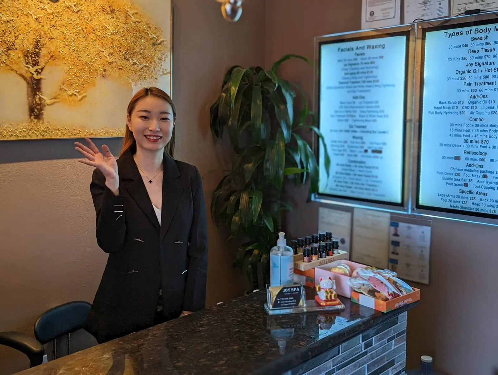 Joy Spa front desk in Las Vegas with a team member waving beside the lighted service menu